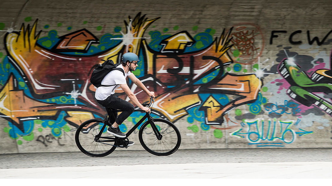 Conquer the City - Innsbruck Andi Wittmann cycling in front of a graffiti