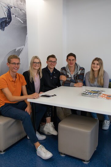Drei Männer und zwei Frauen sitzen an einem Tisch und lächeln in die Kamera.