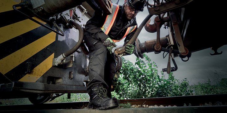  Une personne équipée de chaussures de sécurité MACCROSSROAD travaillant entre deux wagons sur des rails en extérieur