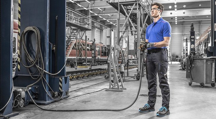 mężczyzna w okularach, odzieży i obuwiu ochronnym obsługuje urządzenie pneumatyczne