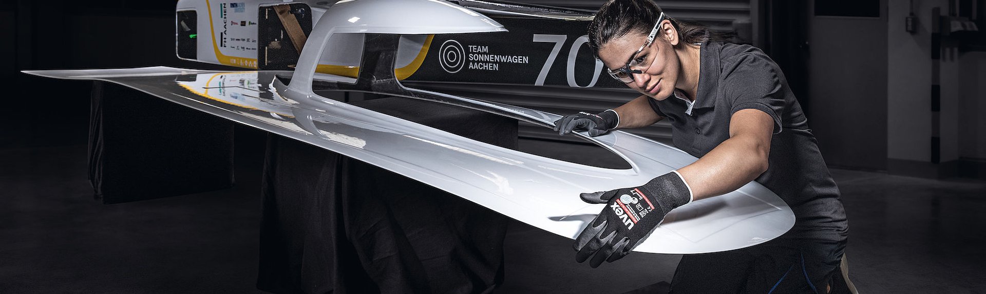 Kobieta w okularach i rękawicach ochronnych kontroluje jakość wykonania powłoki lakierniczej