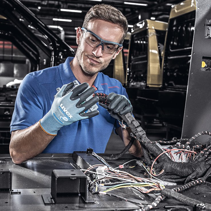 mężczyzna w niebieskich rękawicach ochronnych montuje wiązkę kablową