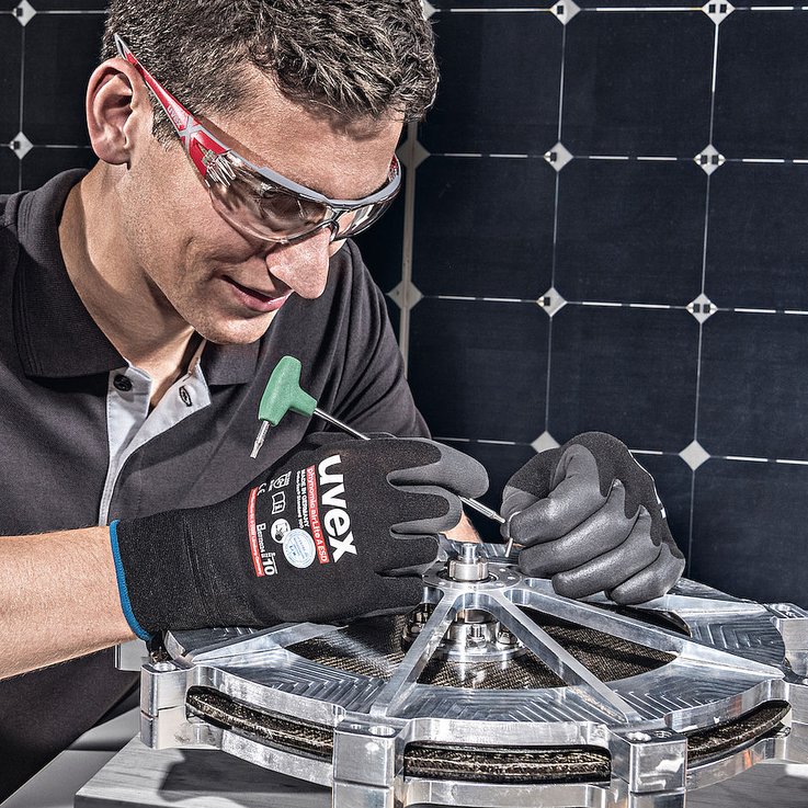 mężczyzna w czarnych rękawiacach ochronnych montuje małe, metalowe elementy 