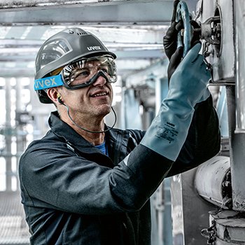 mężczyzna ubrany w rękawice chemiczne, gogle i hełm odkręca duży zawór